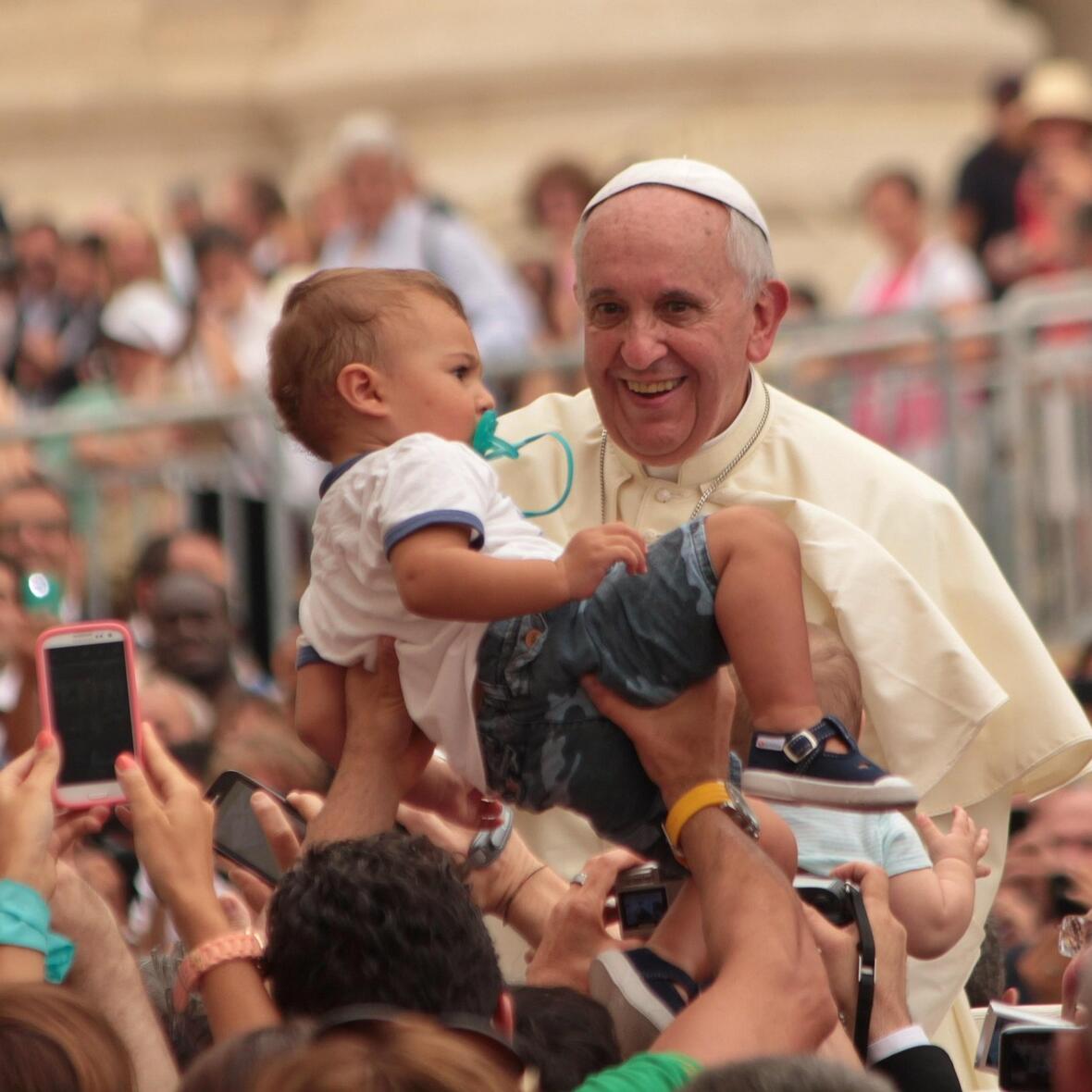 Papst Franziskus wird bei einer Generalaudienz auf dem Petersplatz ein Kind  zum Segnen entgegengehalten.