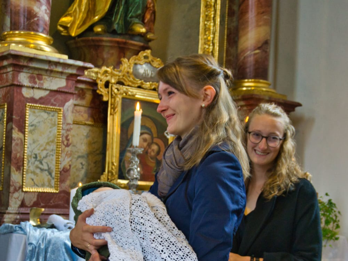 Eine Frau hält ein Baby, das in weiß gekleidet ist in einer Kirche.