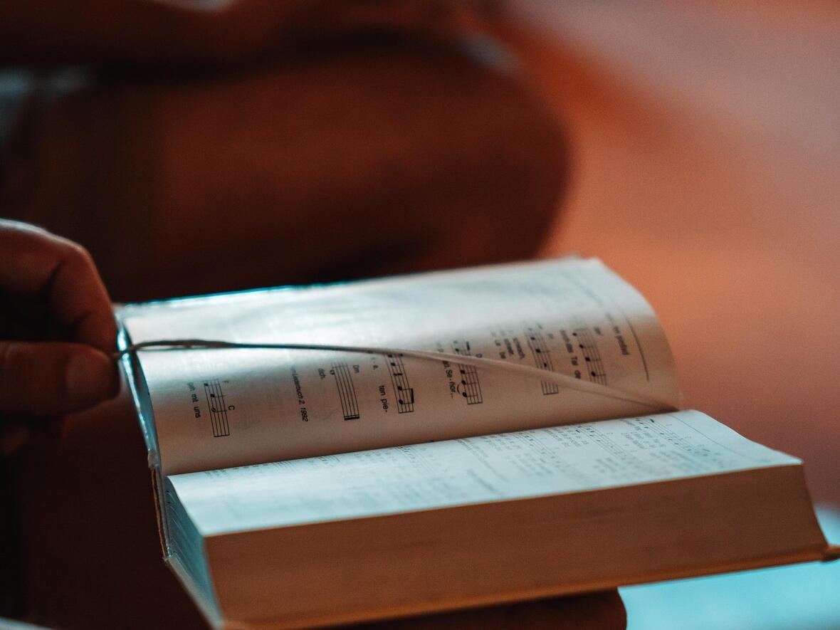Ein Mann hält ein Liederbuch in der Hand. Im Hintergrund sind andere Sänger zu sehen. 