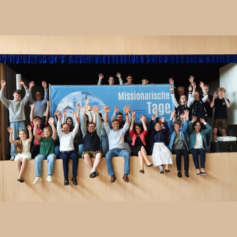 Jugendliche und Erwachsene auf einer Bühne. Im Hintergrund das Plakat der Missionarischen Tage in Baindlkirch