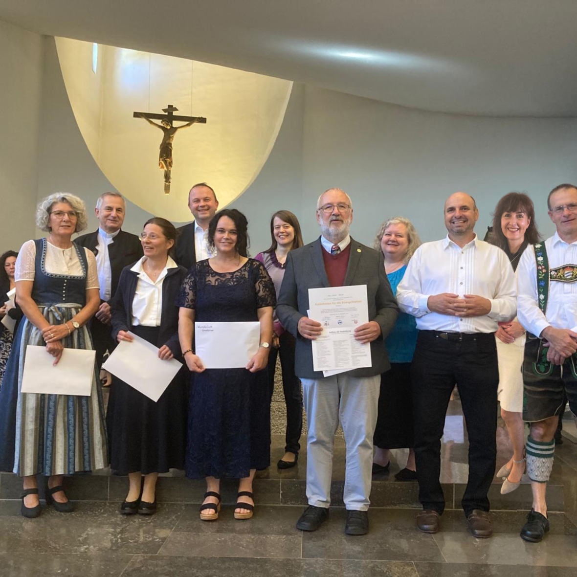 Männer und Frauen stehen lächelnd vorne in der Kirche, manche mit Dokument in der Hand.