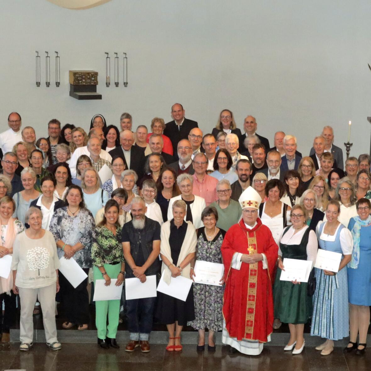 Eine große Personengruppe steht lächelnd vorne in der Kirche, darunter ein Bischof.
