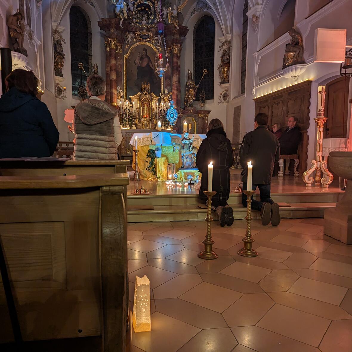 Altarraum mit betenden Menschen. Kerzen und Lichter erzeugen eine stimmungsvolle Atmosphäre