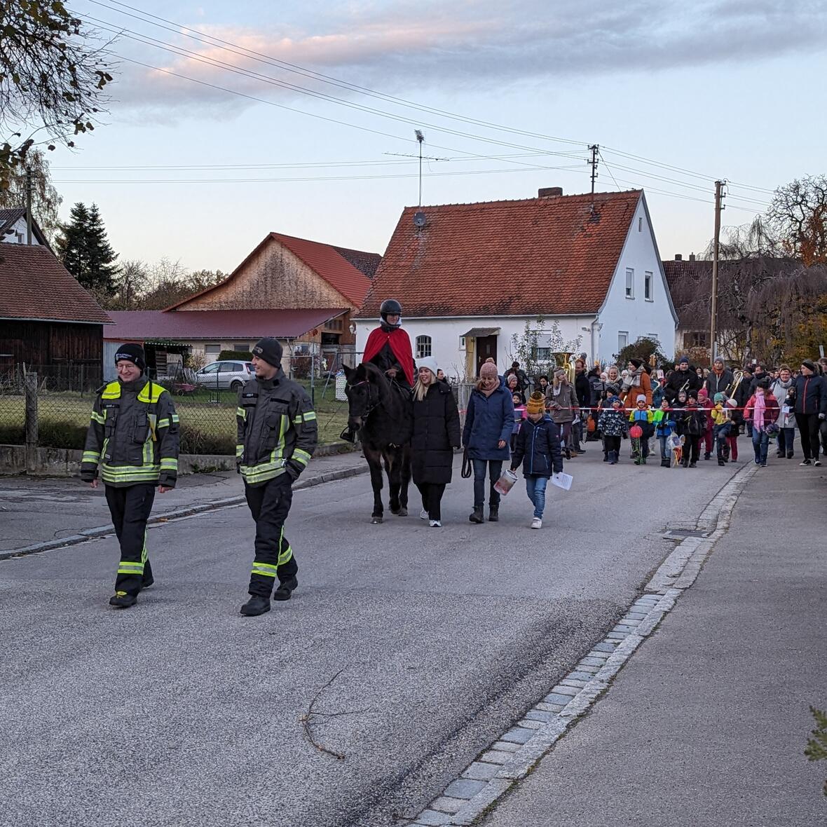 Feuerwehrleute begleiten den Martinsumzug mit einem Reiter mit rotem Mantel und Pferd