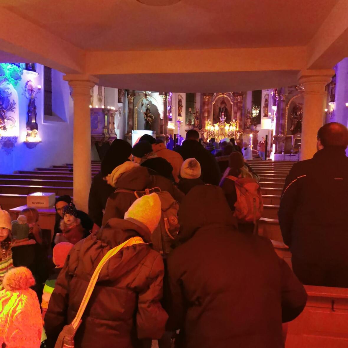 Eine Schlange winterlich gekleideter Menschen steht im Mittelgang einer Kirche und wartet. 