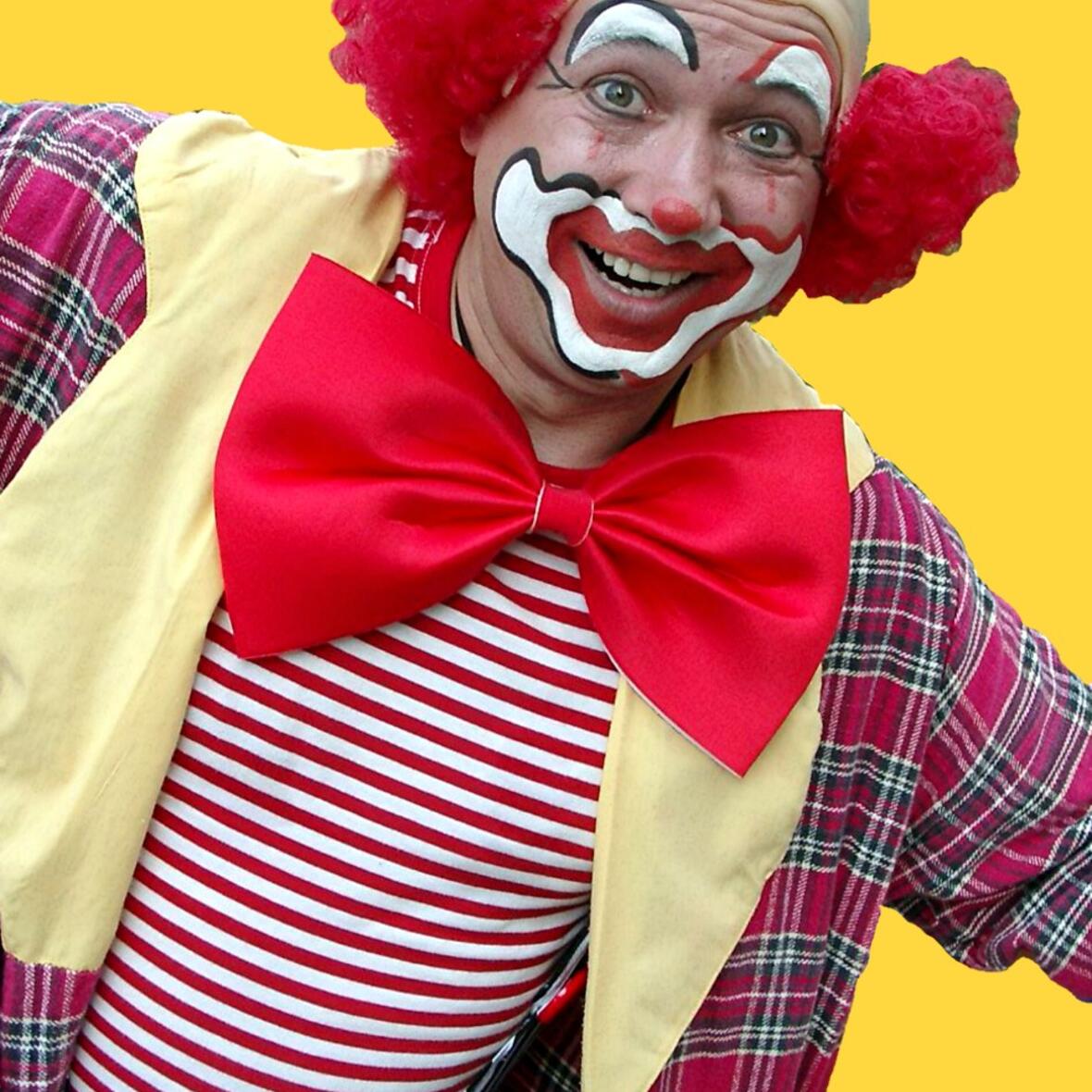 Ein schwarz-weiß-rot geschminkter Clown im Brustbild mit großer roter Fliege auf gelbem Hintergrund.