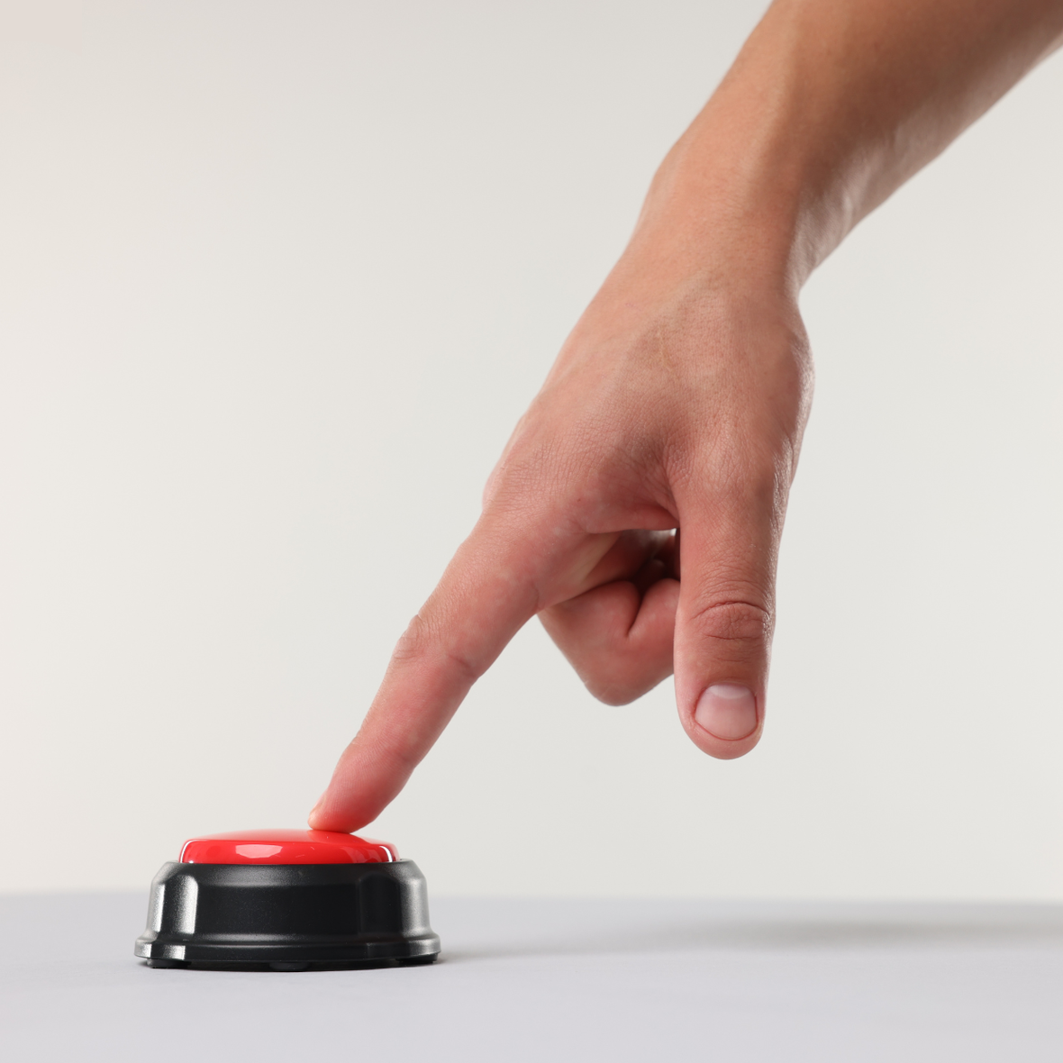 Ein Zeigefinger drückt auf einen roten Knopf, der auf einem weißen Tisch angebracht ist. 