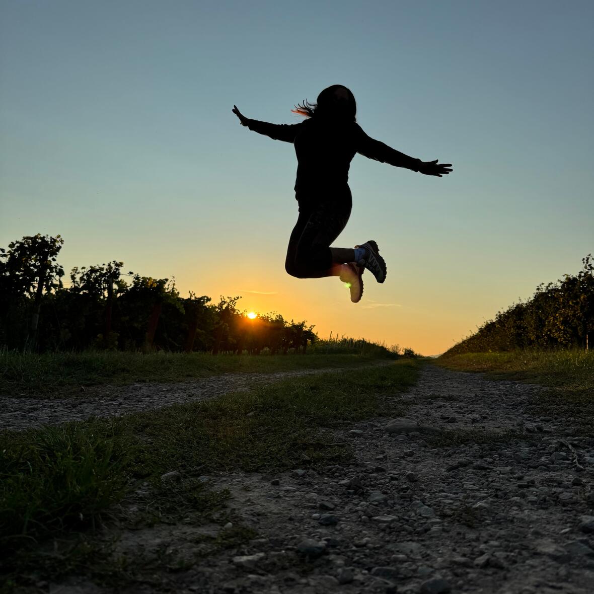 Silhouette einer Frau, die in die Luft springt, im Hintergrund die untergehende Sonne