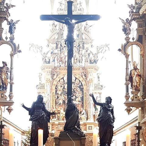 Kreuzigungsgruppe auf der Altarinsel in der Augsburger Basilika St. Ulrich und Afra, im Hintergrund ist schemenhaft der Hochaltar der Kirche 1zu sehen. 