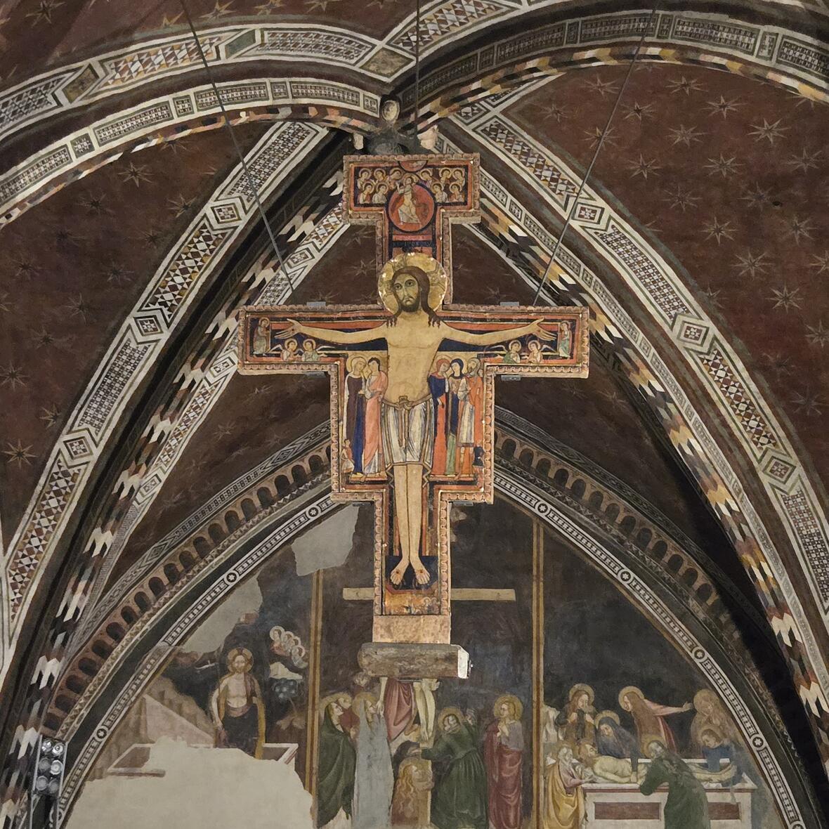 Das bekannte und detailreiche Franziskuskreuz von San Damiano hängt in einer Seitenkapelle von Santa Chiara von der Decke über einem Altar. Am deutlichsten und größten ist Christus mit den Wundmalen auf dem Kreuz zu erkennen. 