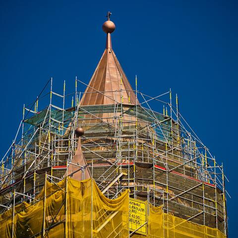 Ein Kirchturm ist außen von einem Gerüst umgeben. 