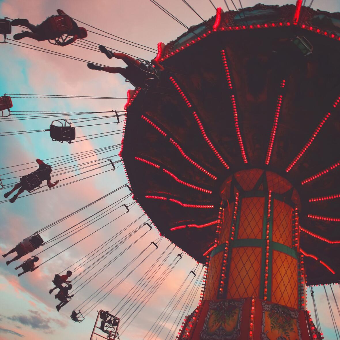 Kirchweih Blick von unten hoch auf ein rotbeleuchtetes Kettenkarussel, das sich im Abendrothimmel dreht.