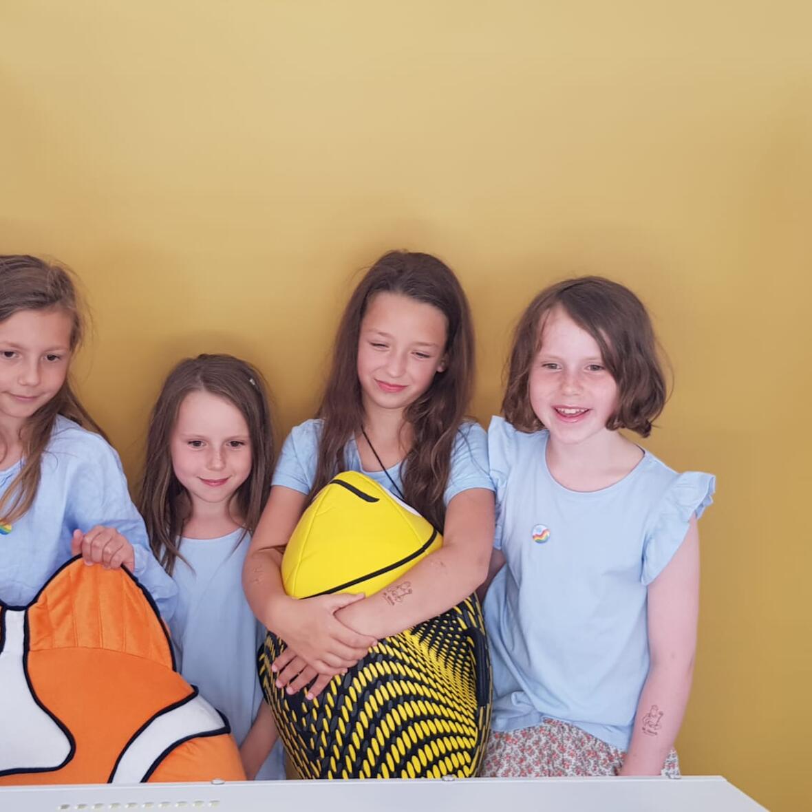 Kinder stehen vor der Fotoboxwand und halten zwei Fische in den Händen. 