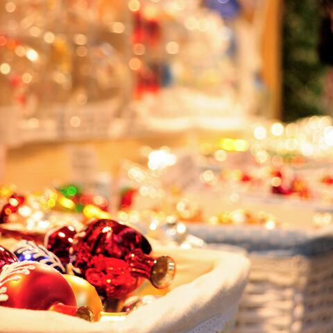 Geflochtene Körbe mit Christbaumschmuck vor einer warm erleuchteten Bude. 