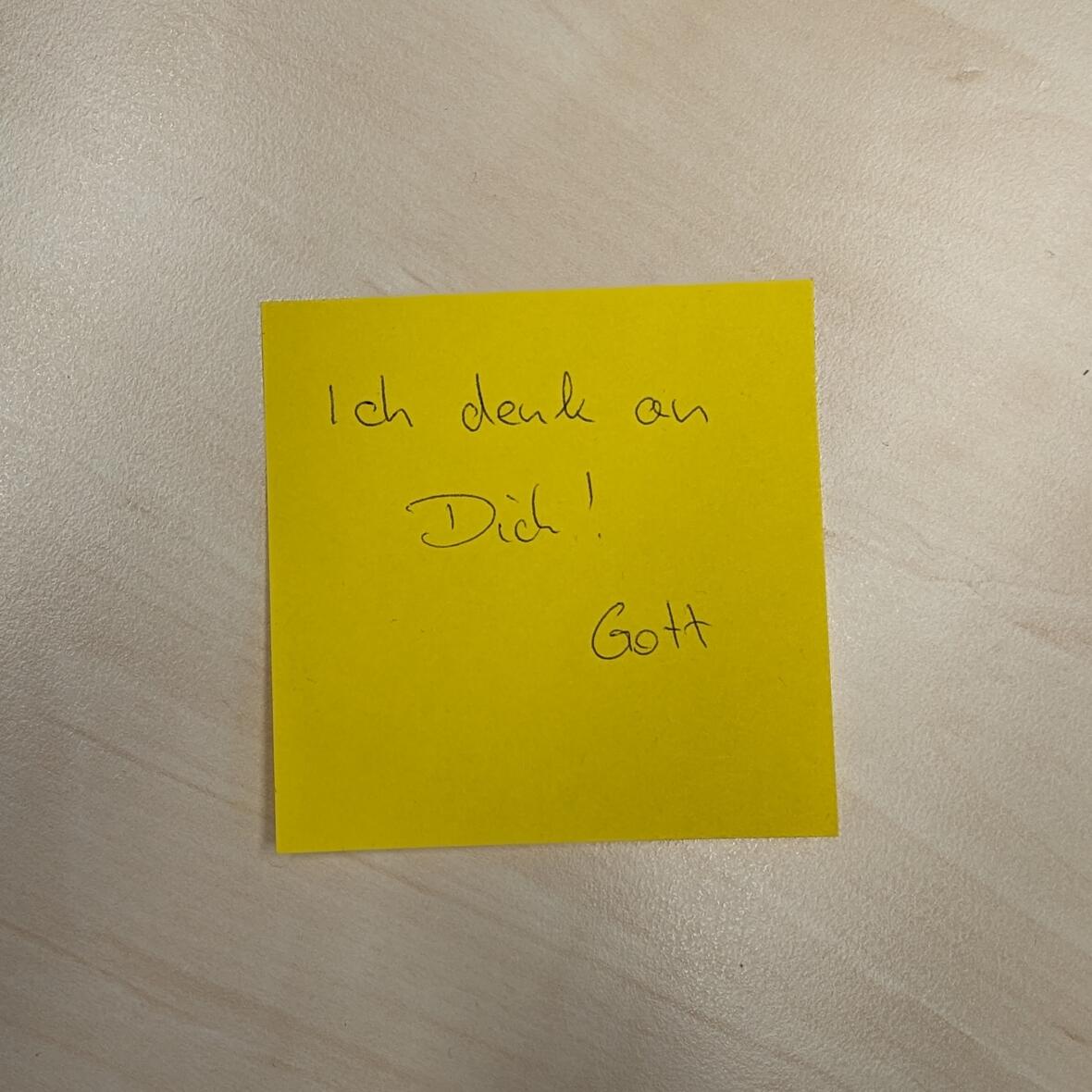 Auf einem Holztisch klebt ein gelber Postit: Ich denk an dich! Gott