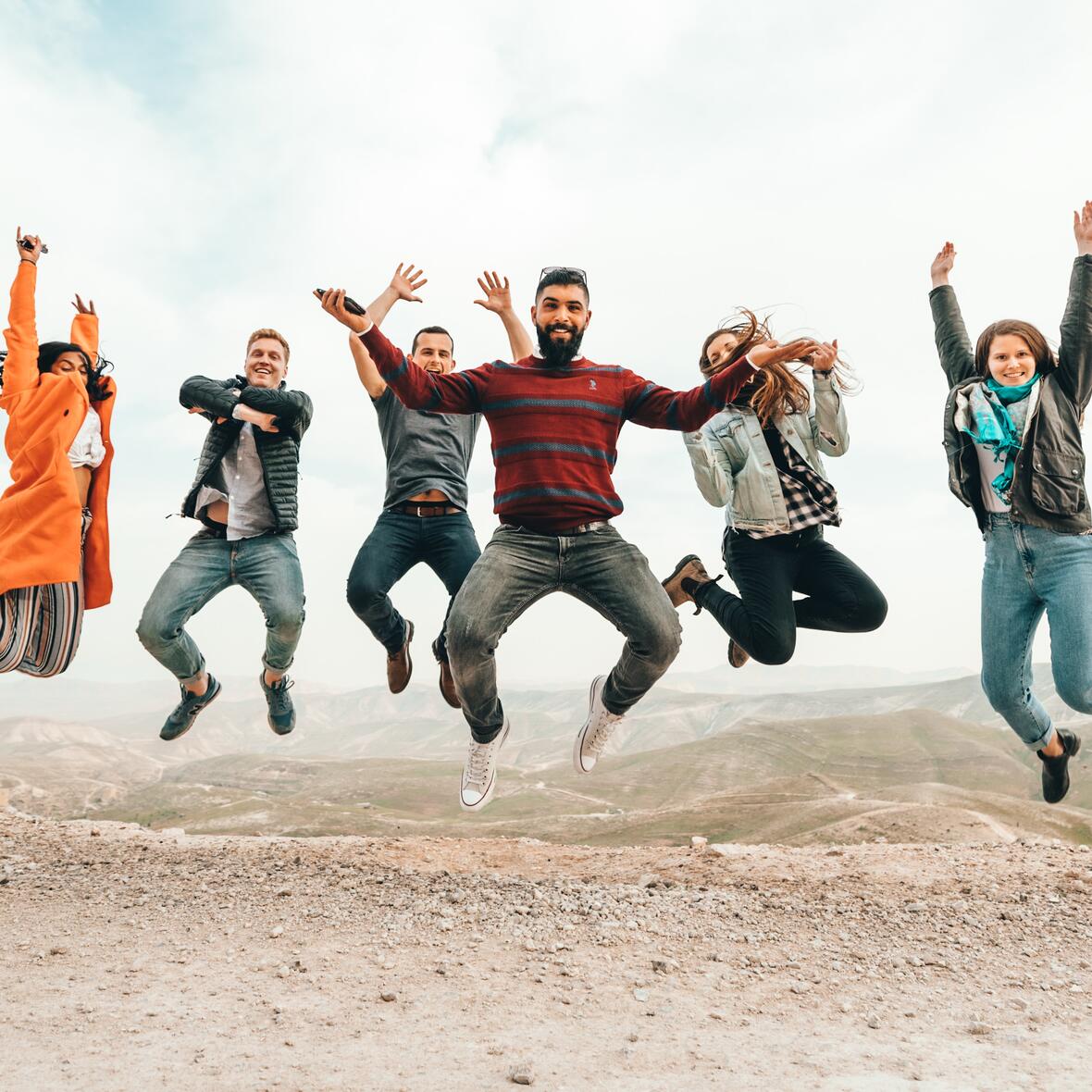 Viele junge Menschen springen in der Wüste in die Luft.