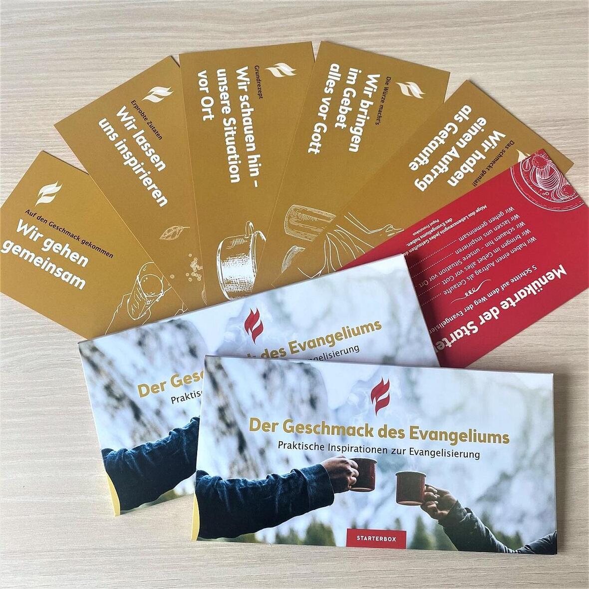 Auf einem braunen Tisch liegen die verschiedenfarbigen Impulskarten der Starterbox zusammen mit der Hülle auf der steht: "Der Geschmack des Evangeliums - Praktische Inspirationen zur Evangelisierung