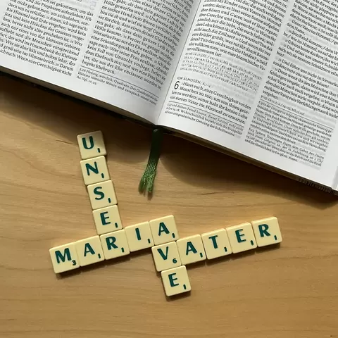 Unterhalb einer Bibel ist mit Scrabble Steinen das Begriffspaar: "Vater unser, Ave Maria" gelegt