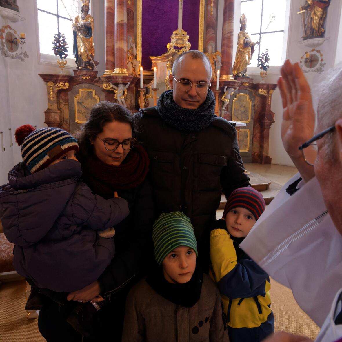 Eine junge Familie mit Papa, Mama und drei Kindern empfängt den Segen eines Priesters