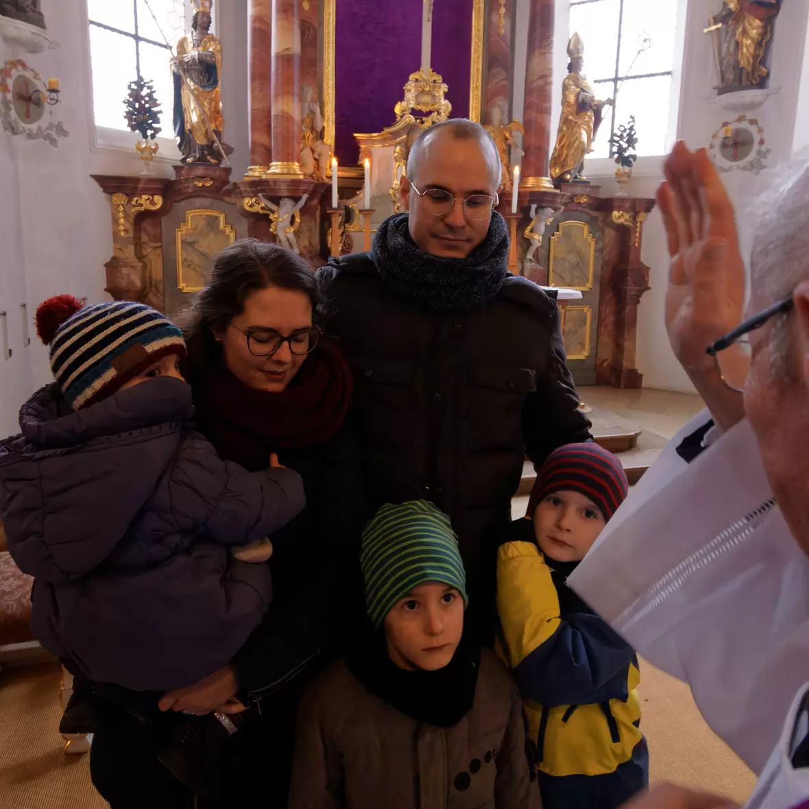 Eine junge Familie mit Papa, Mama und drei Kindern empfängt den Segen eines Priesters