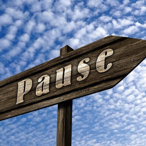 Vor einem Himmel mit Schäfchenwolken ist ein braunes Holzschild mit der Aufschrift Pause zu sehen. 