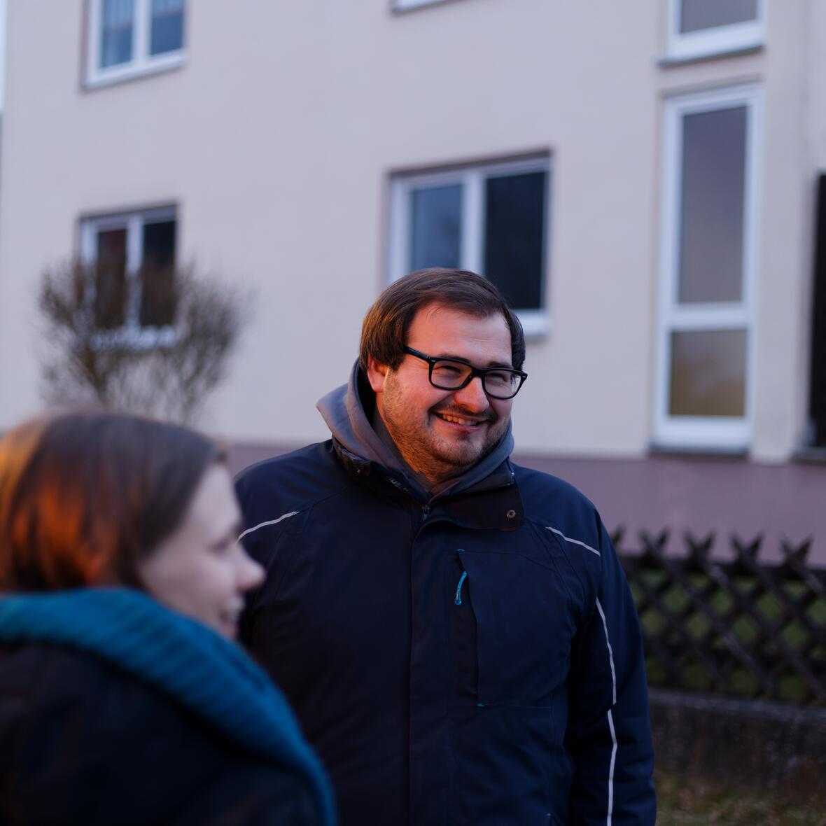 Ein fröhlicher junger Mann steht vor einem lächelndem Mädchen.