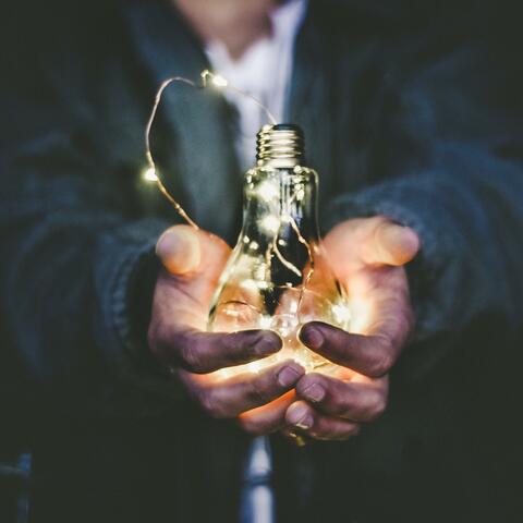 Ein Mann hält eine Glühbirne in der Hand, in der eine Lichterkette leuchtet.