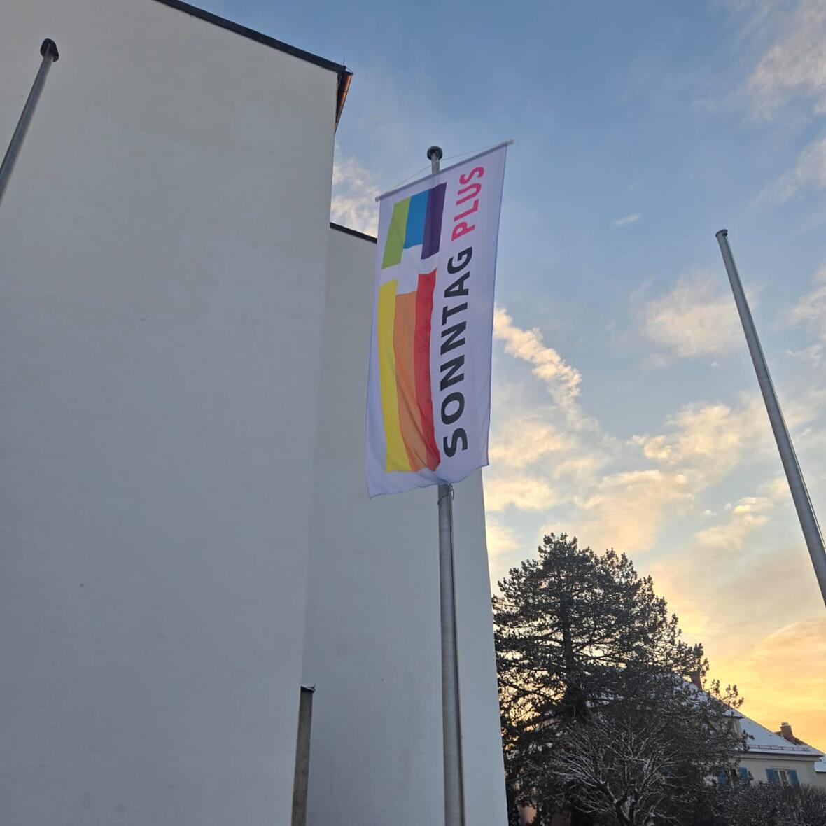 An einem Fahnenmast hängt eine Fahne mit dem Schriftzug: Sonntag Plus
