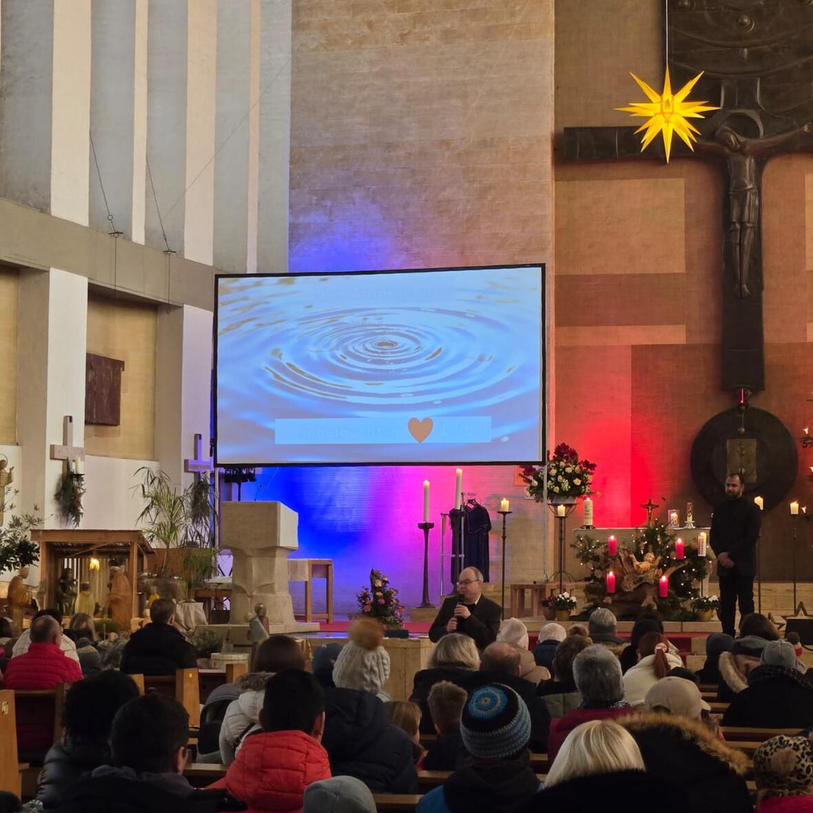 Kirchenraum mit Menschen, die auf eine Leinwand blicken. 