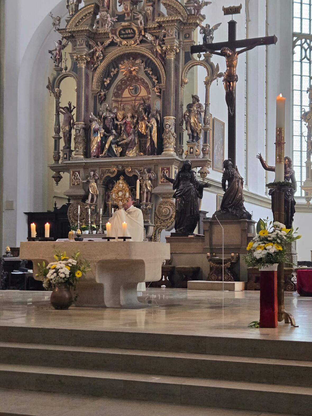 Ein Priester spendet mit einer Monstranz den Segen  im Altarraum von St. Ulrich und Afra, Augsburg