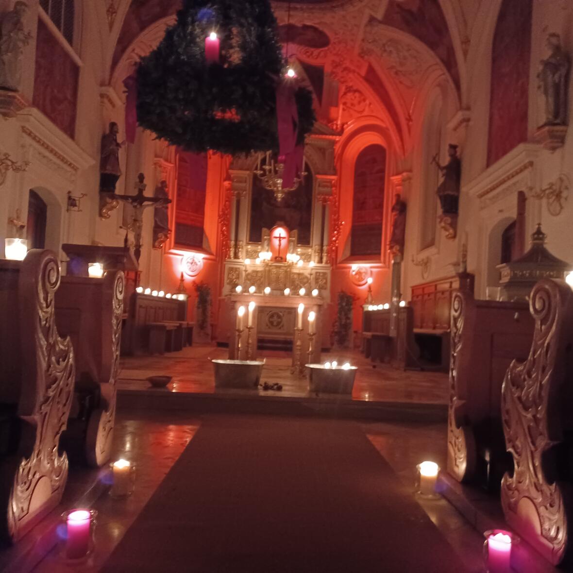 Beleuchteter Altarraum einer Kirche mit Adventskranz