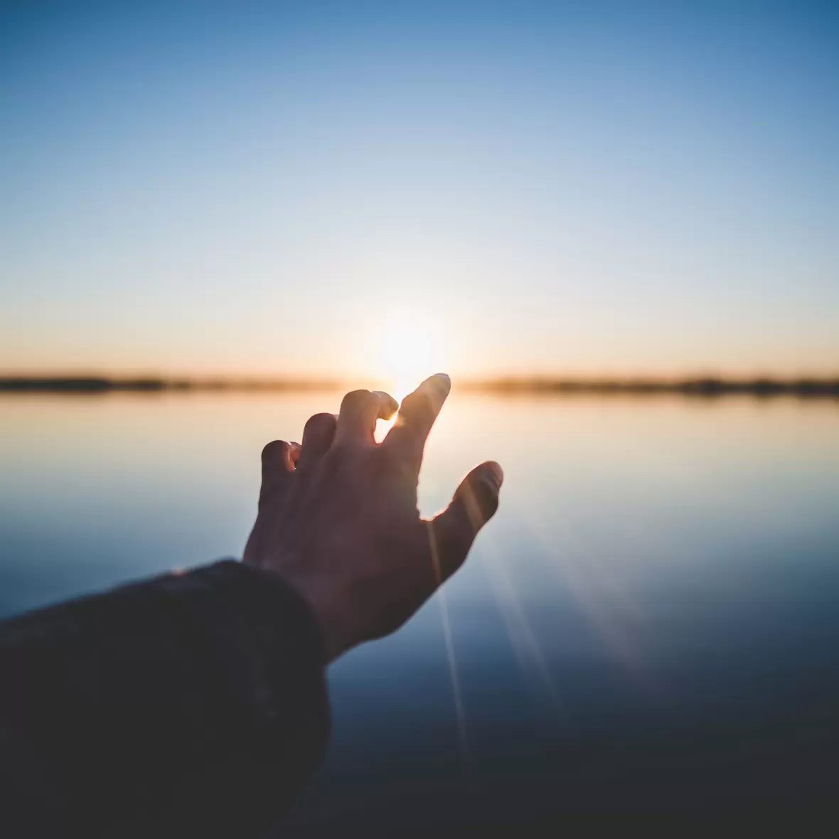 Eine Hand, die auf den Horizont zeigt. Im Hintergrund geht die Sonne auf