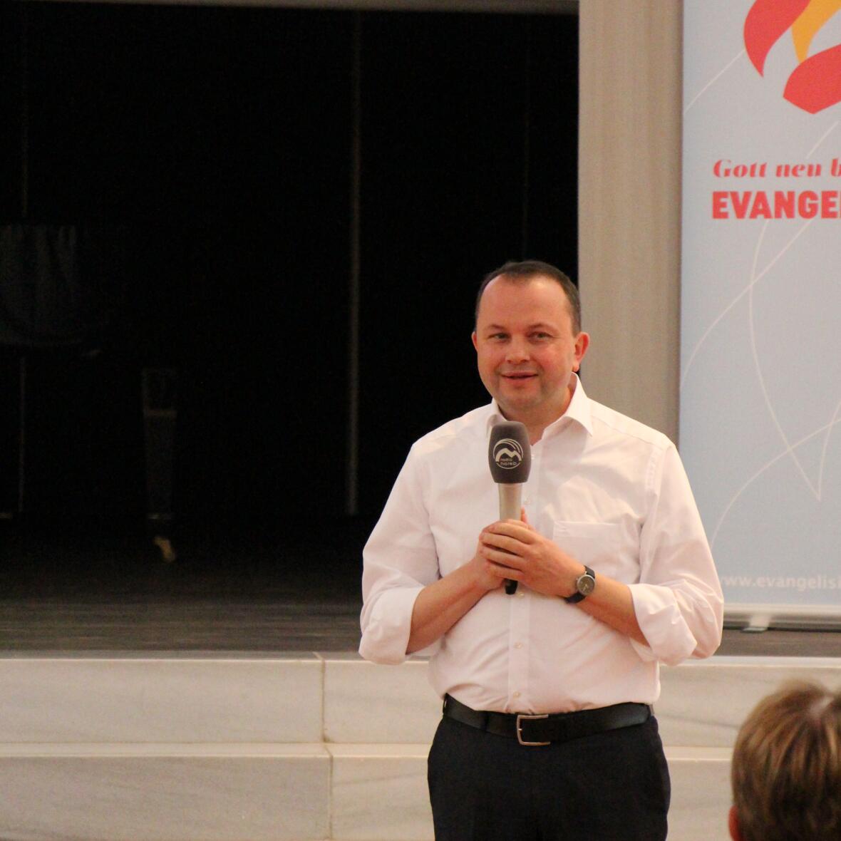 Pfarrer Rimmel spricht vor dem Publikum. Er hält das Mikrophon von Radio Horeb in den Händen 